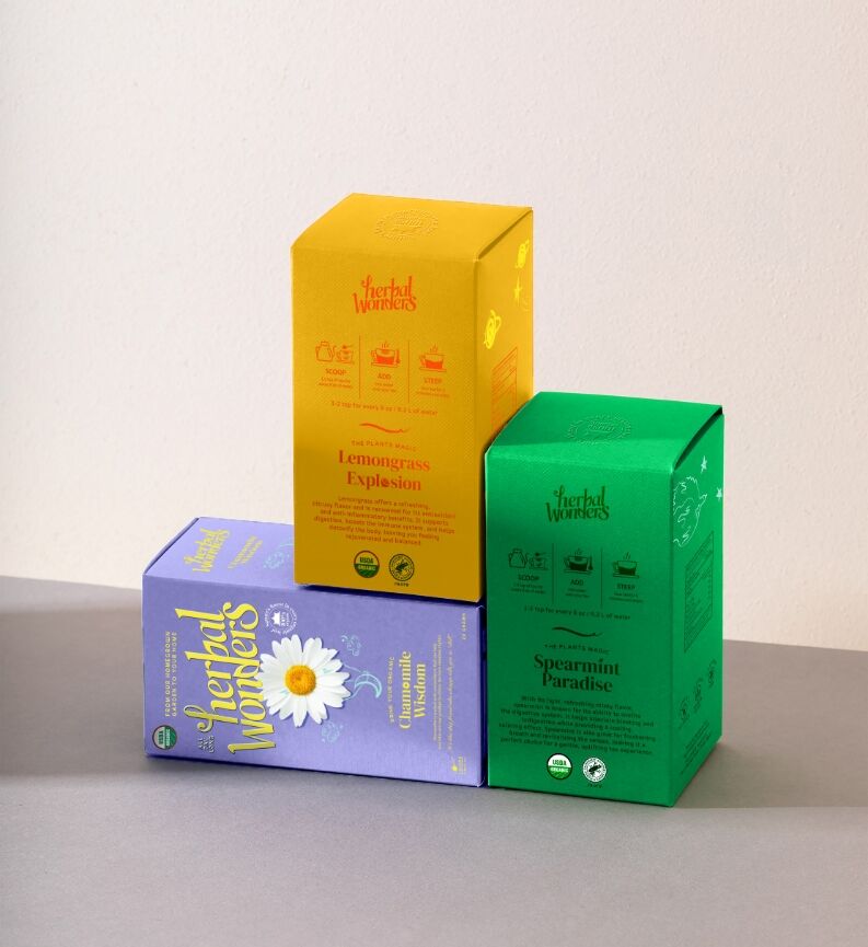 Three Herbal Wonders tea boxes — yellow, green and purple — arranged on a neutral studio background